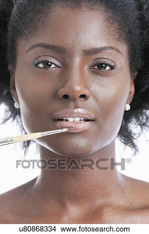 Picture - Close-up portrait of young woman applying lip gloss with brush. Fotosearch