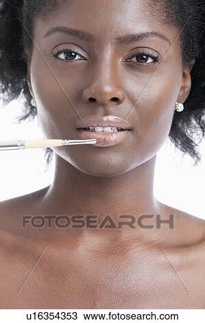 Stock Image - Close-up portrait of young woman applying lip gloss with brush. Fotosearch
