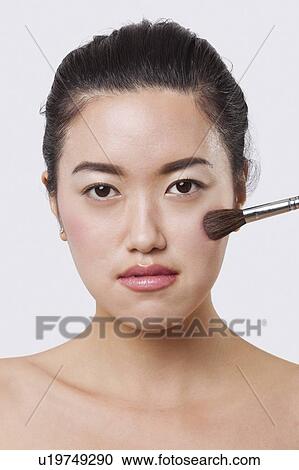 Stock Image - Close-up portrait of young woman applying blush over white background. Fotosearch