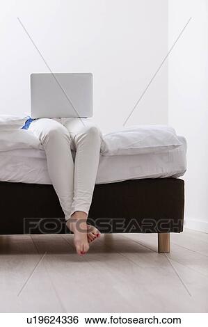 Stock Photograph - Close-up view of Woman using laptop on her bed. Fotosearch