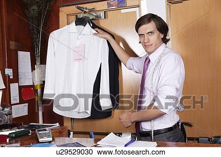 Stock Image - Confident owner with shirts at counter. Fotosearch