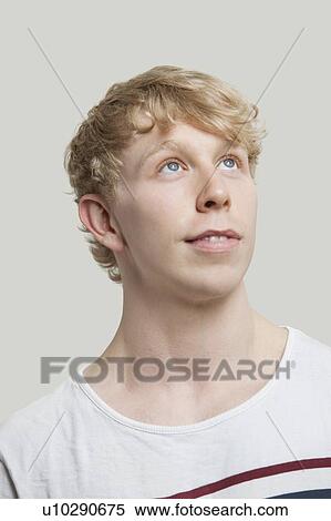 Stock Photography - Contemplative young man standing against gray background. Fotosearch