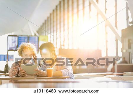 Couple using digital tablet while waiting for their flight in airport with lens flare View Large Photo Image Stock Image - Couple using digital tablet while waiting for their flight in airport with lens flare. Fotosearch