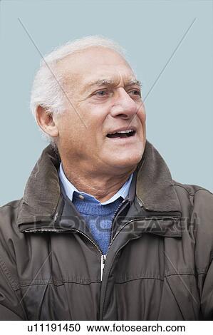 Stock Image - Elderly man looking away against blue background. Fotosearch