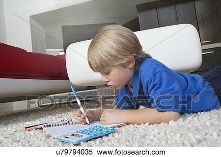 Elementary age boy writing in book while lying down on rug in house View Large Photo Image Stock Photography - Elementary age boy writing in book while lying down on rug in house. Fotosearch