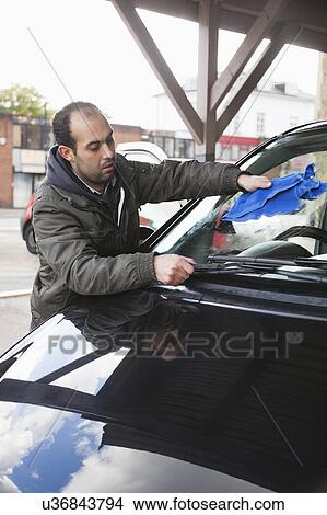 Picture - Employee wiping vehicle windscreen in car wash. Fotosearch