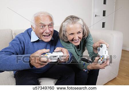 Stock Image - Enthusiastic senior couple playing video game at home. Fotosearch