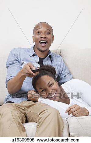 Stock Photo - Excited young African American couple watching TV. Fotosearch