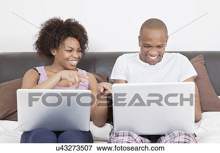 Stock Photo - Excited young African American couple using laptops on bed. Fotosearch