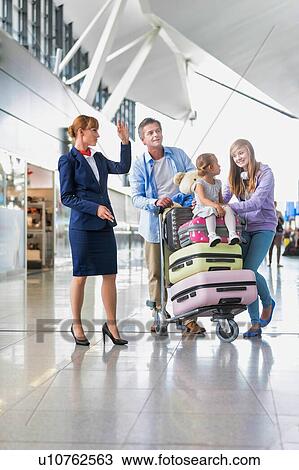 Stock Image - Family on holiday asking for assistance with airport staff in airport with lens flare in background. Fotosearch