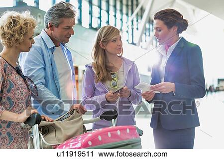 Stock Image - Family on holiday asking for assistance with airport staff in airport with lens flare in background. Fotosearch