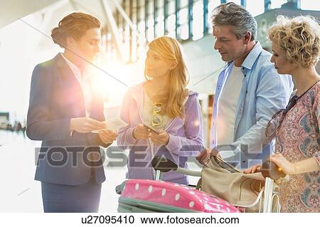 Stock Image - Family on holiday asking for assistance with airport staff in airport with lens flare in background. Fotosearch