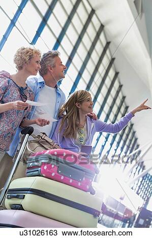 Stock Image - Family on holiday looking at their flights on monitor in airport. Fotosearch