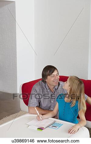 Stock Photograph - Father and daughter looking at each other while doing homework together. Fotosearch