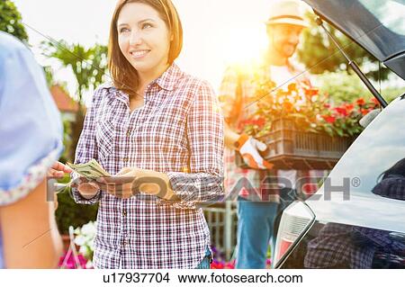Female customer giving cash payment to the shop owner against mature gardener putting flowers on car trunk View Large Photo Image Picture - Female customer giving cash payment to the shop owner against mature gardener putting flowers on car trunk. Fotosearch