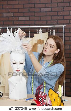 Stock Photography - Female fashion designer adjusting feather fascinator on mannequin. Fotosearch