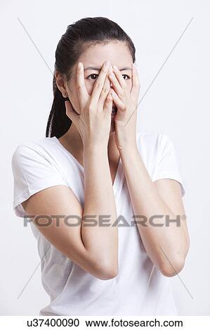 Stock Image - Frightened young woman with hands on face against white background. Fotosearch