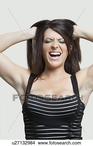 Picture - Frustrated young woman with hands in hair over gray background. Fotosearch