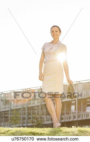 Full length of happy young businesswoman holding footwear in office lawn View Large Photo Image Stock Image - Full length of happy young businesswoman holding footwear in office lawn. Fotosearch