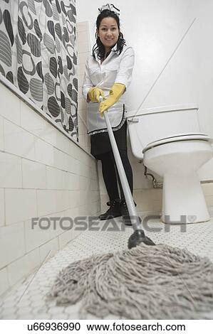 Stock Image - Full length portrait of maidservant cleaning bathroom floor. Fotosearch