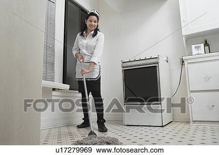 Stock Photo - Full length portrait of young housemaid cleaning floor with mop. Fotosearch