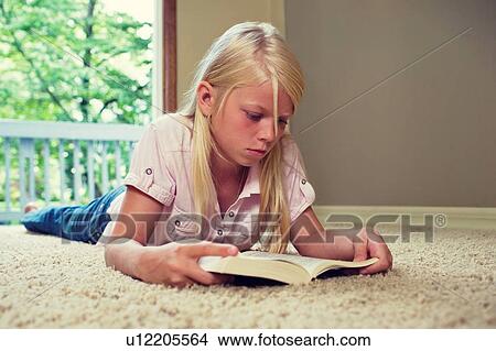 Picture - Girl lying on carpet, reading book. Fotosearch