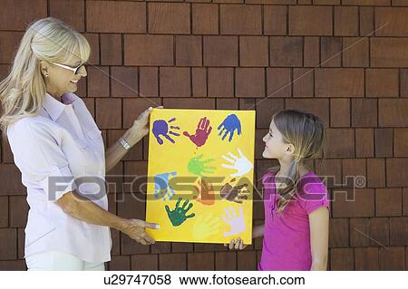 Stock Photo - Grandmother and granddaughter showing colorful multiple hand prints against brick wall. Fotosearch