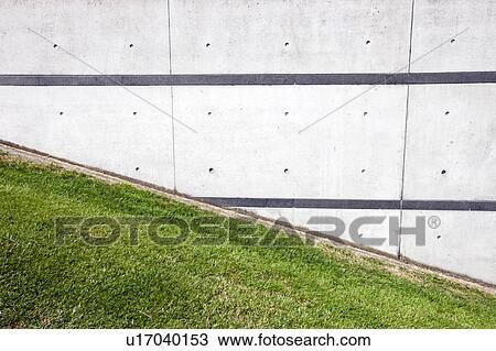 Stock Image - Green grass slope next to brick wall. Fotosearch