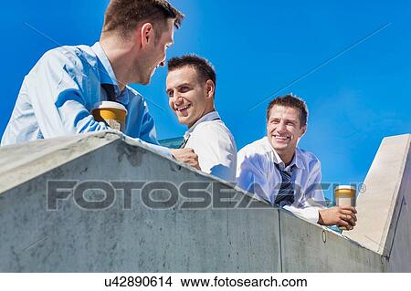 Picture - Group of businessmen standing and talking while drinking coffee during break. Fotosearch
