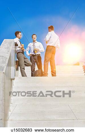 Stock Image - Group of businessmen standing and talking while drinking coffee during break. Fotosearch