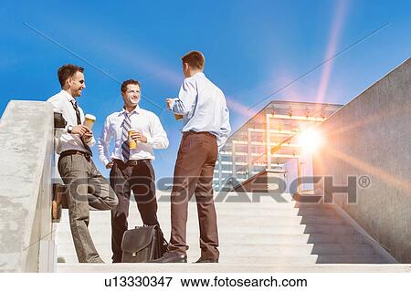 Group of businessmen standing and talking while drinking coffee during break View Large Photo Image Stock Photo - Group of businessmen standing and talking while drinking coffee during break. Fotosearch