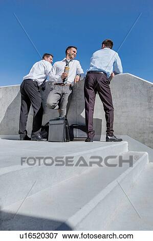 Group of businessmen standing and talking while drinking coffee during break View Large Photo Image Stock Photo - Group of businessmen standing and talking while drinking coffee during break. Fotosearch