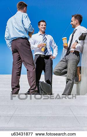 Group of businessmen standing and talking while drinking coffee during break View Large Photo Image Stock Photo - Group of businessmen standing and talking while drinking coffee during break. Fotosearch