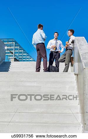 Group of businessmen standing and talking while drinking coffee during break View Large Photo Image Stock Photograph - Group of businessmen standing and talking while drinking coffee during break. Fotosearch