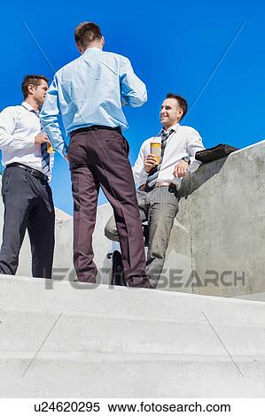 Stock Photography - Group of businessmen standing and talking while drinking coffee during break. Fotosearch