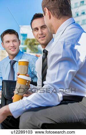 Stock Image - Group of colleagues sitting and talking while drinking coffee after work. Fotosearch
