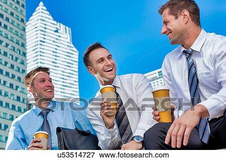 Stock Photo - Group of colleagues sitting and talking while drinking coffee after work. Fotosearch