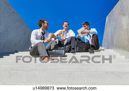 Stock Image - Group of handsome businessman sitting on stairs while talking during break . Fotosearch