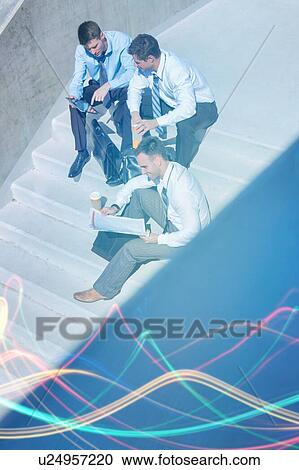 Stock Image - Group of handsome businessman sitting on stairs while preparing business plans during break . Fotosearch