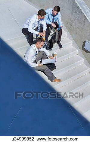Stock Image - Group of handsome businessman sitting on stairs while preparing business plans during break . Fotosearch