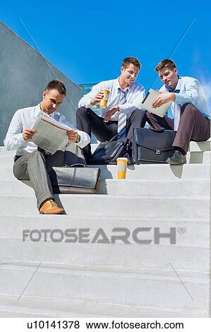 Stock Photo - Group of handsome businessman sitting on stairs while talking during break . Fotosearch