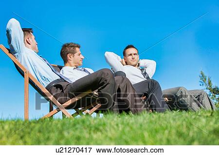 Stock Photo - Group of handsome businessmen relaxing and talking about life while sitting on folding chair at park. Fotosearch