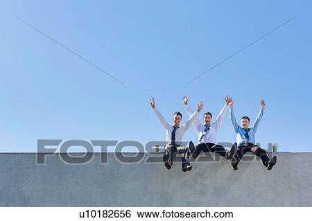 Stock Photograph - Group of handsome businessmen sitting while having fun in office rooftop. Fotosearch