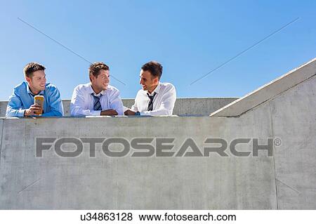 Group of handsome businessmen discussing plans in office rooftop during break View Large Photo Image Stock Photo - Group of handsome businessmen discussing plans in office rooftop during break. Fotosearch
