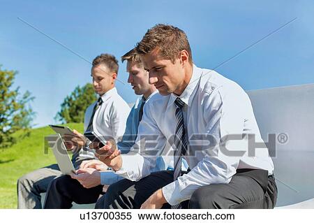 Group of mature businessmen sitting on bench while using gadgets View Large Photo Image Stock Photography - Group of mature businessmen sitting on bench while using gadgets. Fotosearch