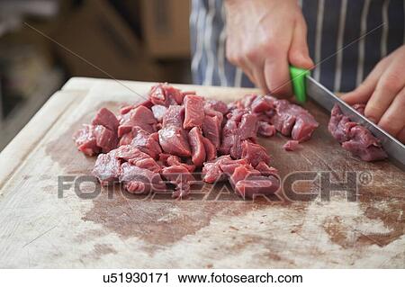 Stock Image - Hands of butcher cutting meat by knife. Fotosearch