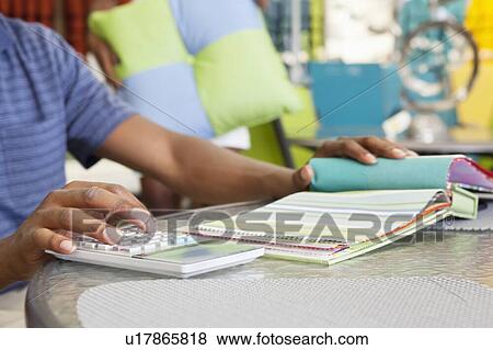 Stock Photo - Hands of male salesperson calculating expenses with swatch on table. Fotosearch