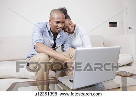 Stock Photo - Happy African American young couple using laptop at home. Fotosearch