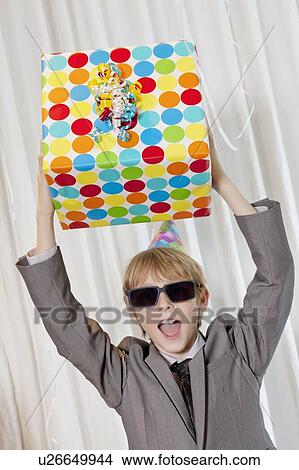 Happy boy wearing sunglasses holding gift aloft while shouting View Large Photo Image Picture - Happy boy wearing sunglasses holding gift aloft while shouting. Fotosearch