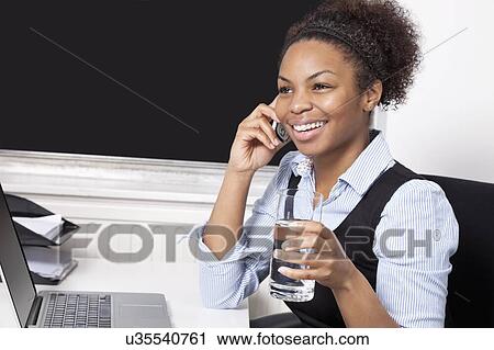 Happy businesswoman using cell phone in front of laptop at desk in office View Large Photo Image Stock Image - Happy businesswoman using cell phone in front of laptop at desk in office. Fotosearch